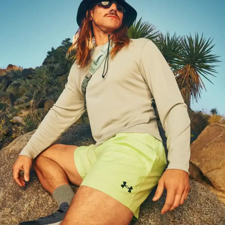 Close-up of an orange trail running shoe on a rocky ledge with a blue sky in the background, person wearing black socks and shorts partially visible beneath the rock.